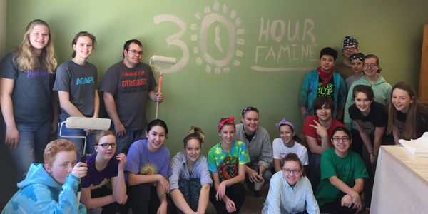 Group of volunteers posing in front of a wall with '30 Hour Famine' painted on it.