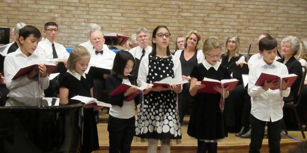 Children and adults singing in a choir performance.