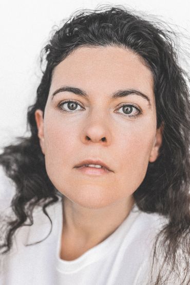 Close-up portrait of a woman with curly hair and a neutral expression.