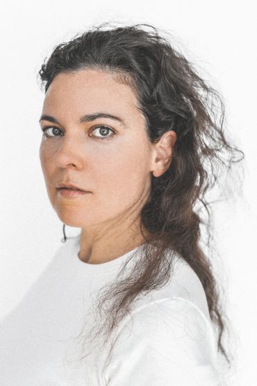 Portrait of a woman with curly hair wearing a white top against a white background.