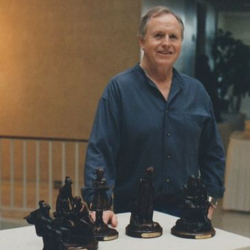 Man smiling behind a table with chess piece sculptures.