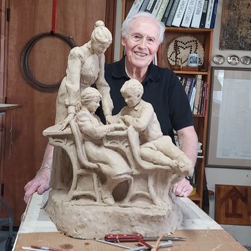 Elderly man proudly presents a detailed clay sculpture of a family scene.