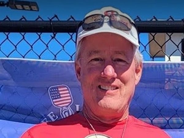 Smiling man in red shirt and white cap outdoors.