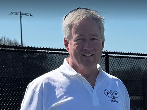 Smiling man in white polo outdoors.