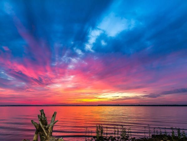 Vibrant sunset with pink, orange, and blue hues over a calm lake.