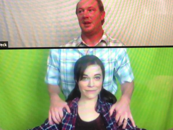 Two people in a split-screen video call, man behind woman with hands on her shoulders.