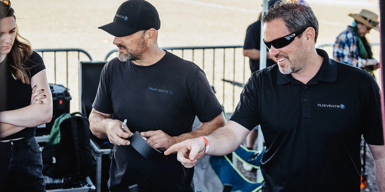 Two men in black Vlievents shirts working with tape and discussing.