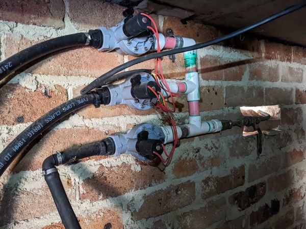 Irrigation solenoid valves installed for easy accessibility above ground on wall of house. 