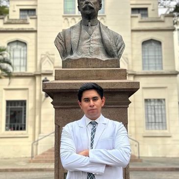 Joven con bata blanca posa frente a un busto de piedra.