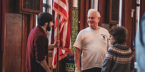 Three people in conversation around an American flag indoors.
