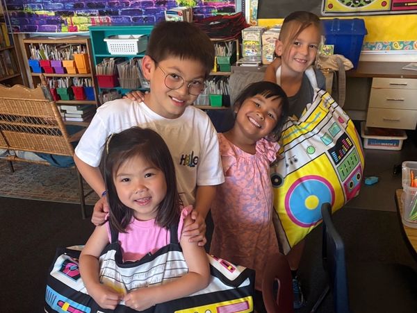 Four children smiling together in a colorful classroom.