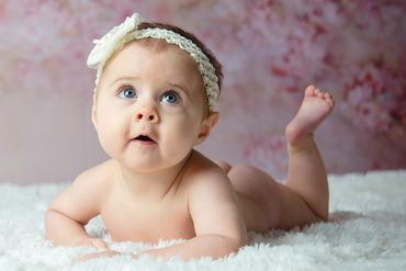 Baby girl poses on belly during her milestone photography session in Austin, Texas photo studio. 