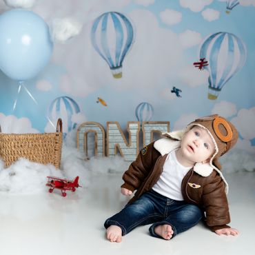 Baby boy poses on blue hot air balloon set for his first birthday photo shoot session. 