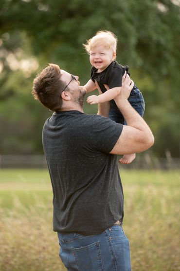 Dad holds smiling baby during outdoor family photoshoot. 