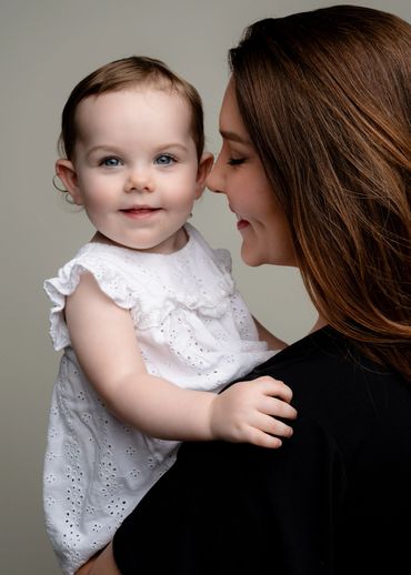 Baby looks at the cake smash photographer while mom hold her during their first birthday photoshoot i