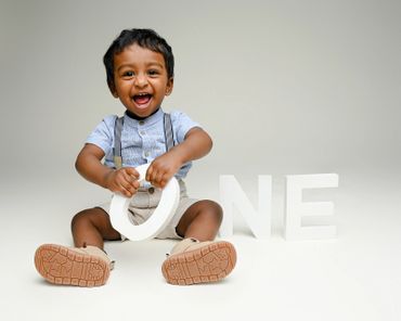 Baby boy holds ONE sign smiling for his cakesmash photoshoot in Austin, Texas.