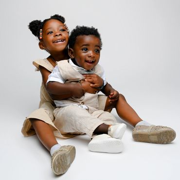 Siblings sit together pose during a cake smash photoshoot in an Austin, photography studio.