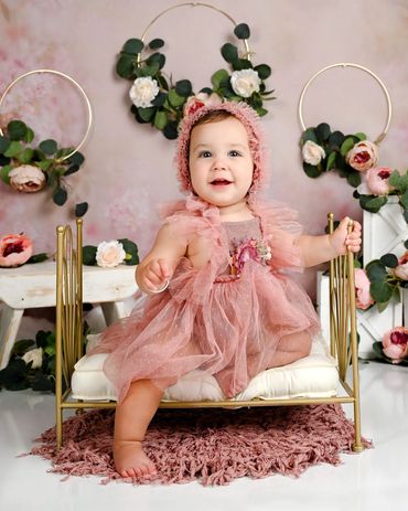 Baby smiles wearing a pink bonnet and gown for her first birthday photoshoot in Austin, Texas. 