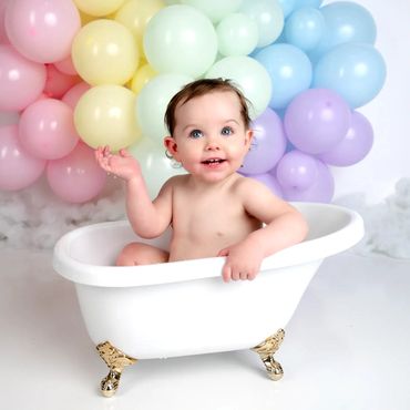 Baby girl sits in small bathtub in front of balloons for her first birthday photoshoot in Austin.