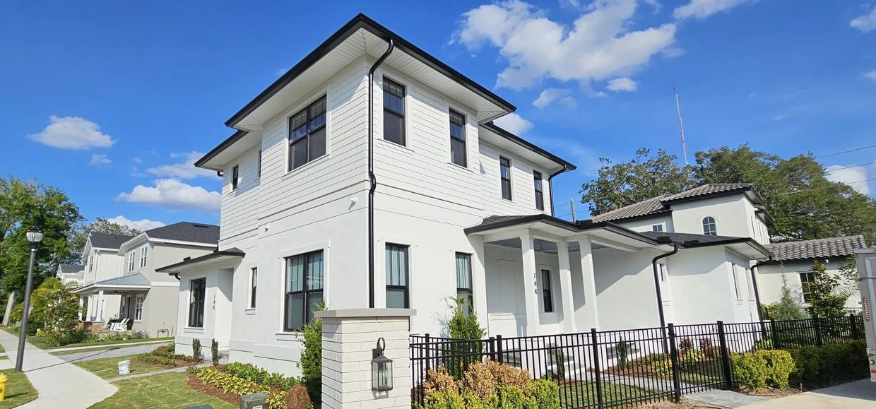 Modern two-story white house with black window frames under a blue sky.
