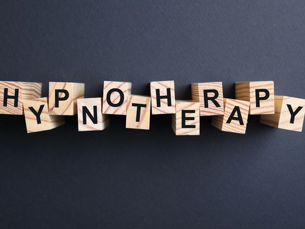 Wooden blocks with word HYPNOTHERAPY on black background, flat lay