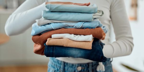 Person holding a neat stack of folded clothes in soft, earthy tones.