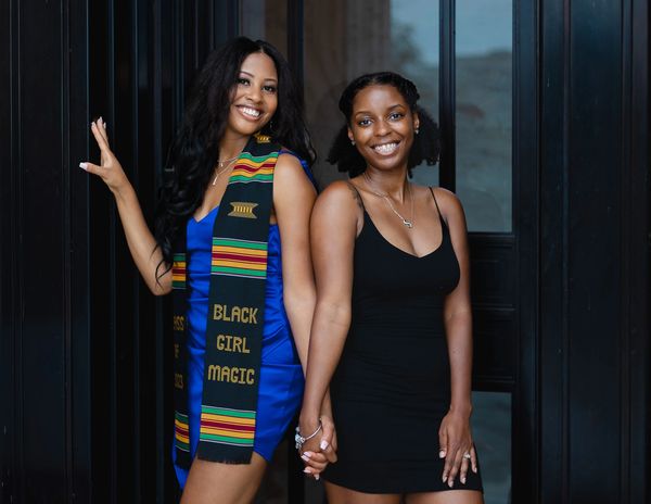 Two women smiling and holding hands, one in a Kente stole.