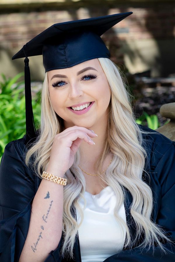 Smiling graduate with tattoo in cap and gown.