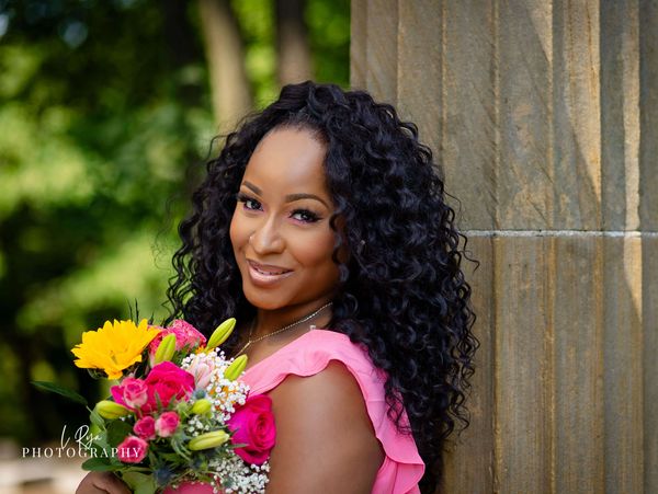 Woman in pink dress holding a bouquet and smiling by a stone pillar.