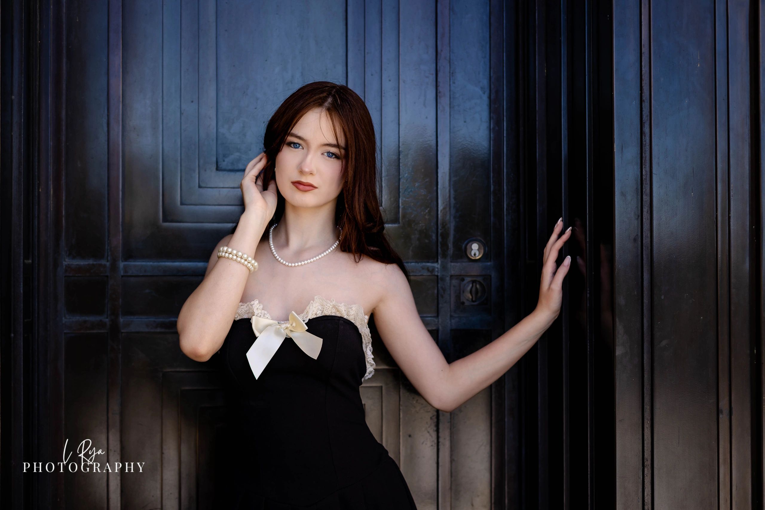 Senior portrait at Cleveland Museum of Art, student in black dress with pearls posing by dark doors.