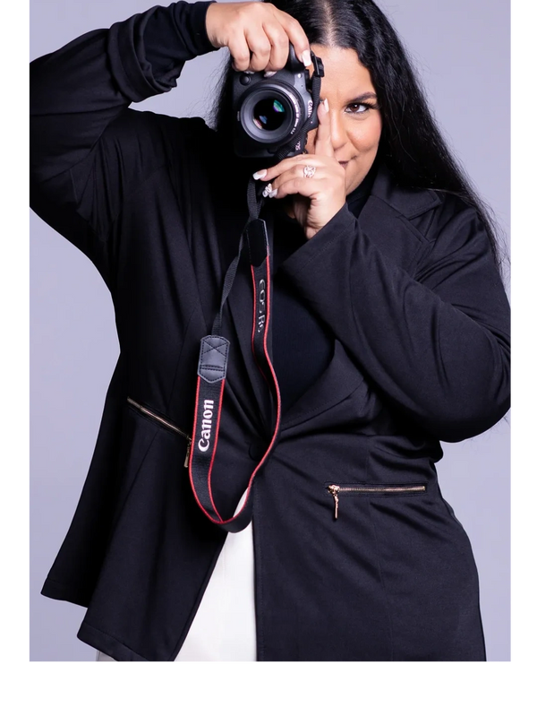 A photographer in a black outfit holds a Canon camera up to her eye, ready to take a picture.