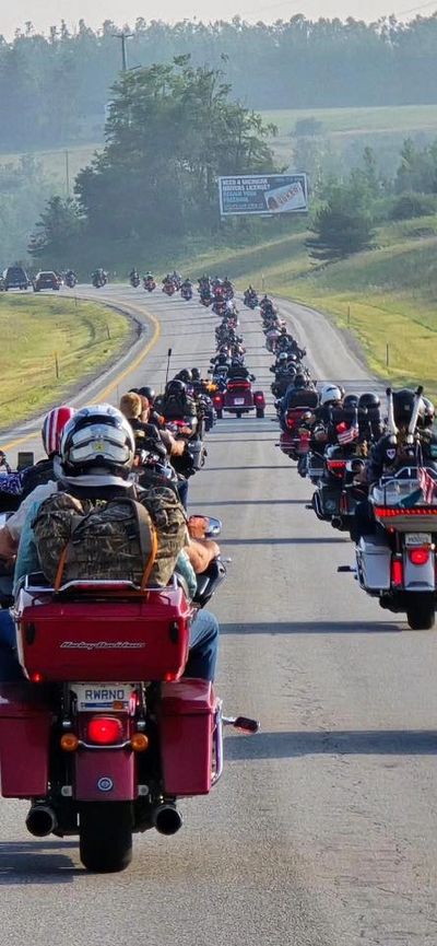 A long line of motorcyclists riding on a highway through a scenic countryside.