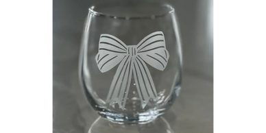 A clear glass tumbler etched with a decorative bow design.