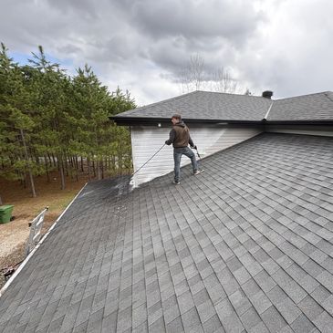 Person power washing a large residential roof under cloudy sky.