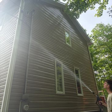 Person pressure washing the side of a house on a sunny day.