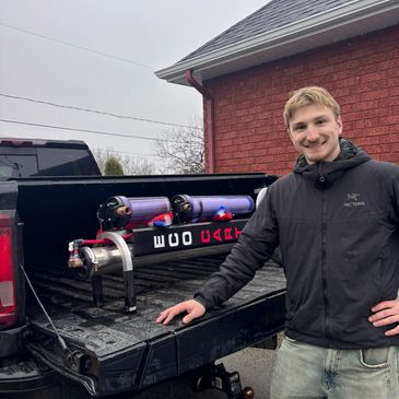 Young man poses with a custom-built mechanical device on a truck bed.