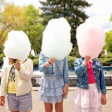 Three children holding cotton candy covering their faces.