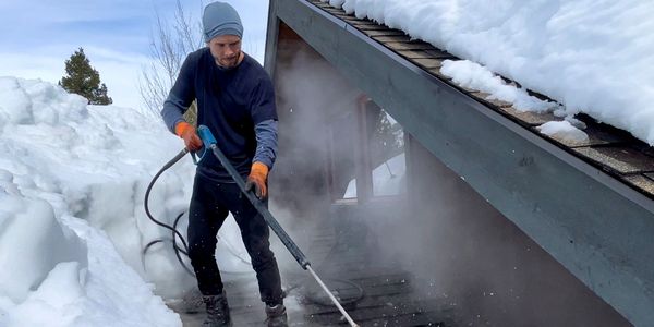 Roof ice dam removal professional on a roof in Bozeman, Montana with a professional ice dam steamer