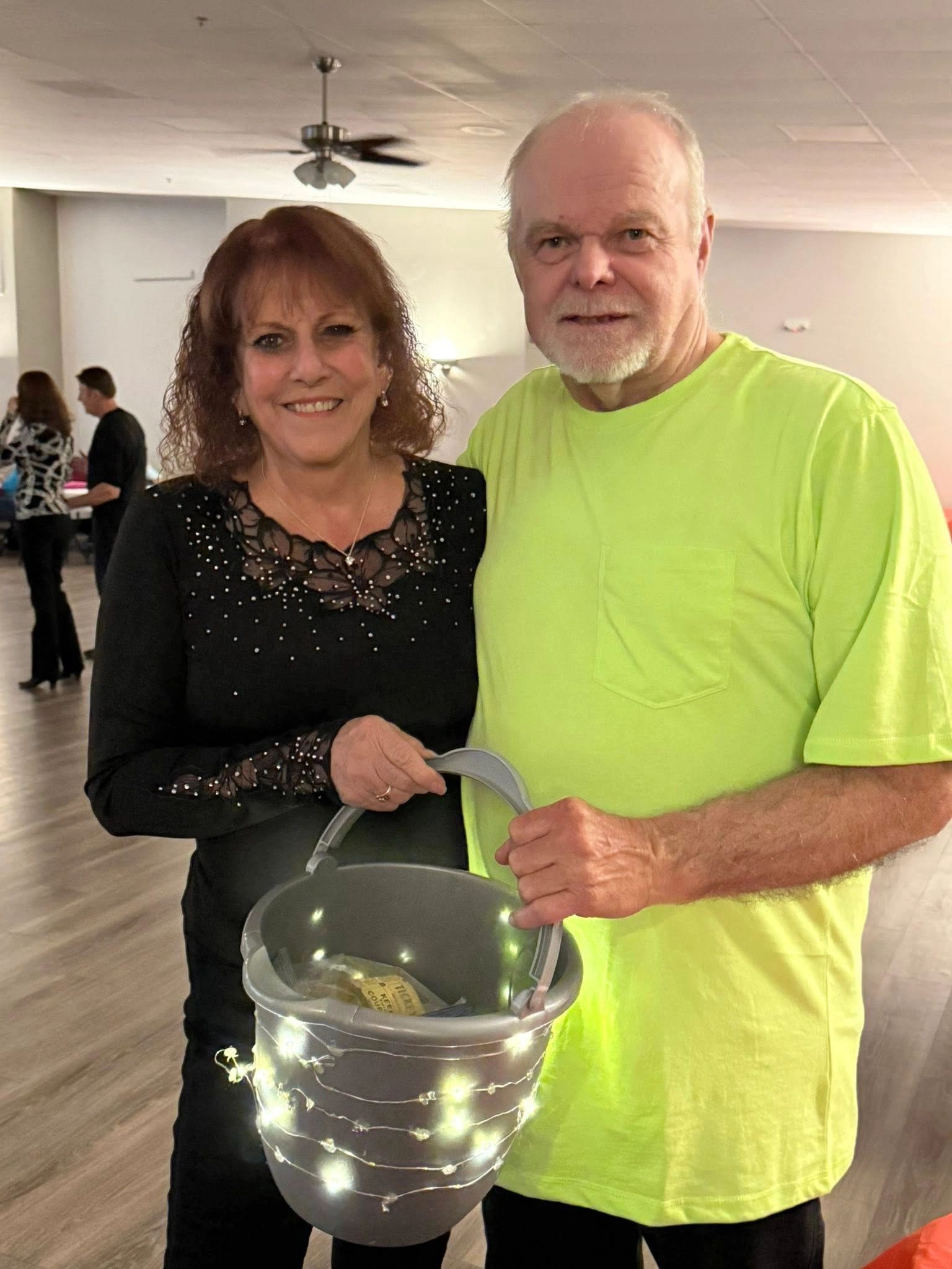 Smiling couple holding a bucket decorated with lights indoors.