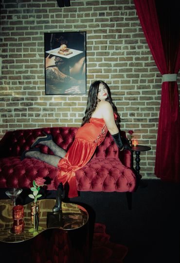 Woman in a red dress posing on a velvet sofa in a stylish room.