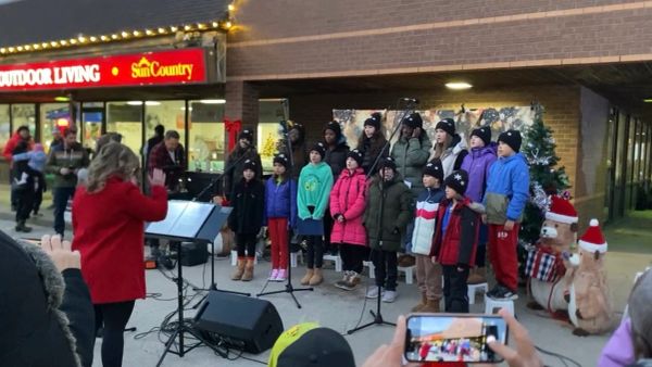 Children choir singing outdoors in winter with conductor.
