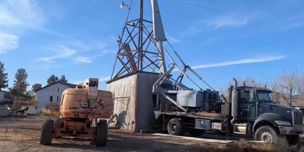Old machinery and a truck near a wooden structure under a blue sky.