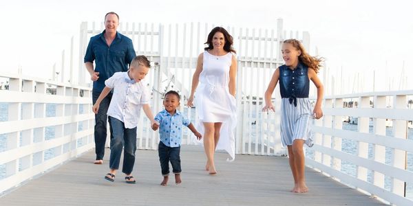 A happy family running barefoot on a pier by the water. The best family photography in San Diego.