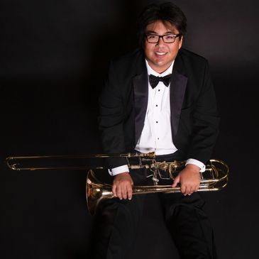 Man in tuxedo holding a trombone in a black background