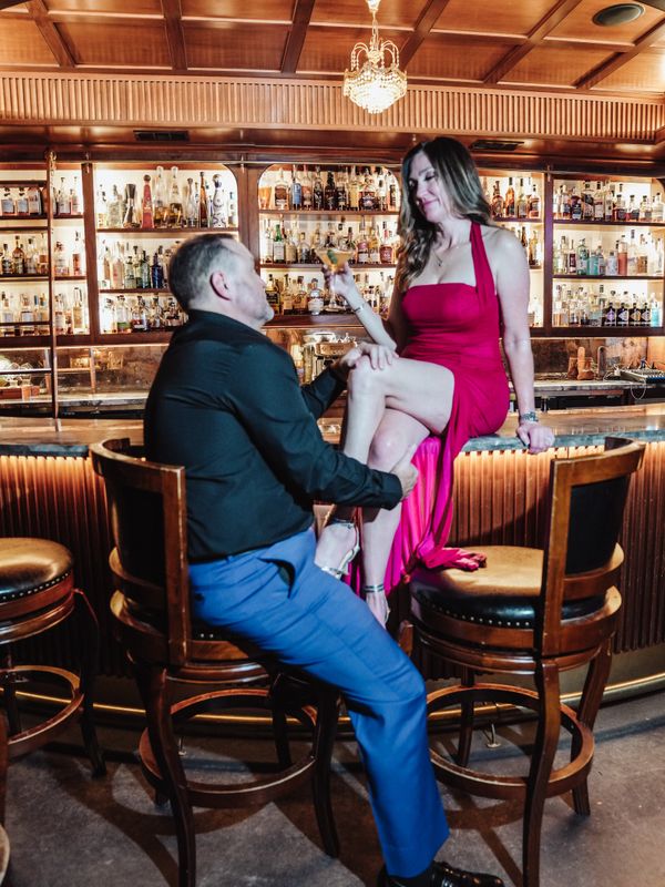 Man kneeling, holding a woman’s leg in a bar with a wooden interior.