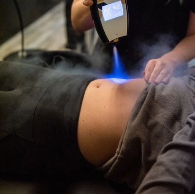 A person receives a cryotherapy treatment on their abdomen with a blue cold spray.