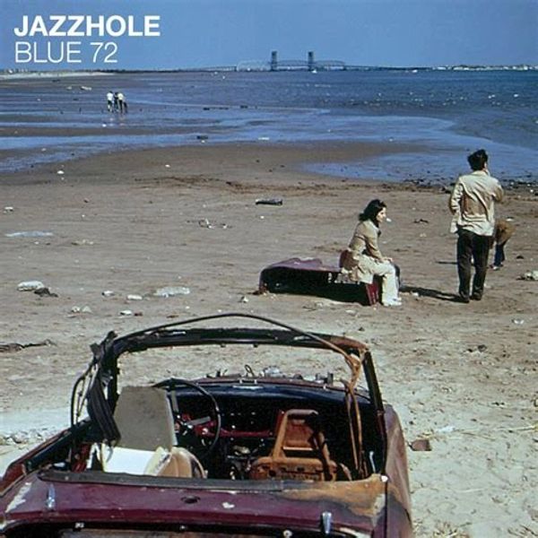 People on a beach with an old car and suitcase.