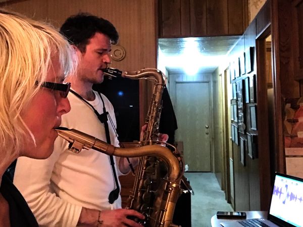 Two people playing saxophones indoors, focused on music on a laptop.