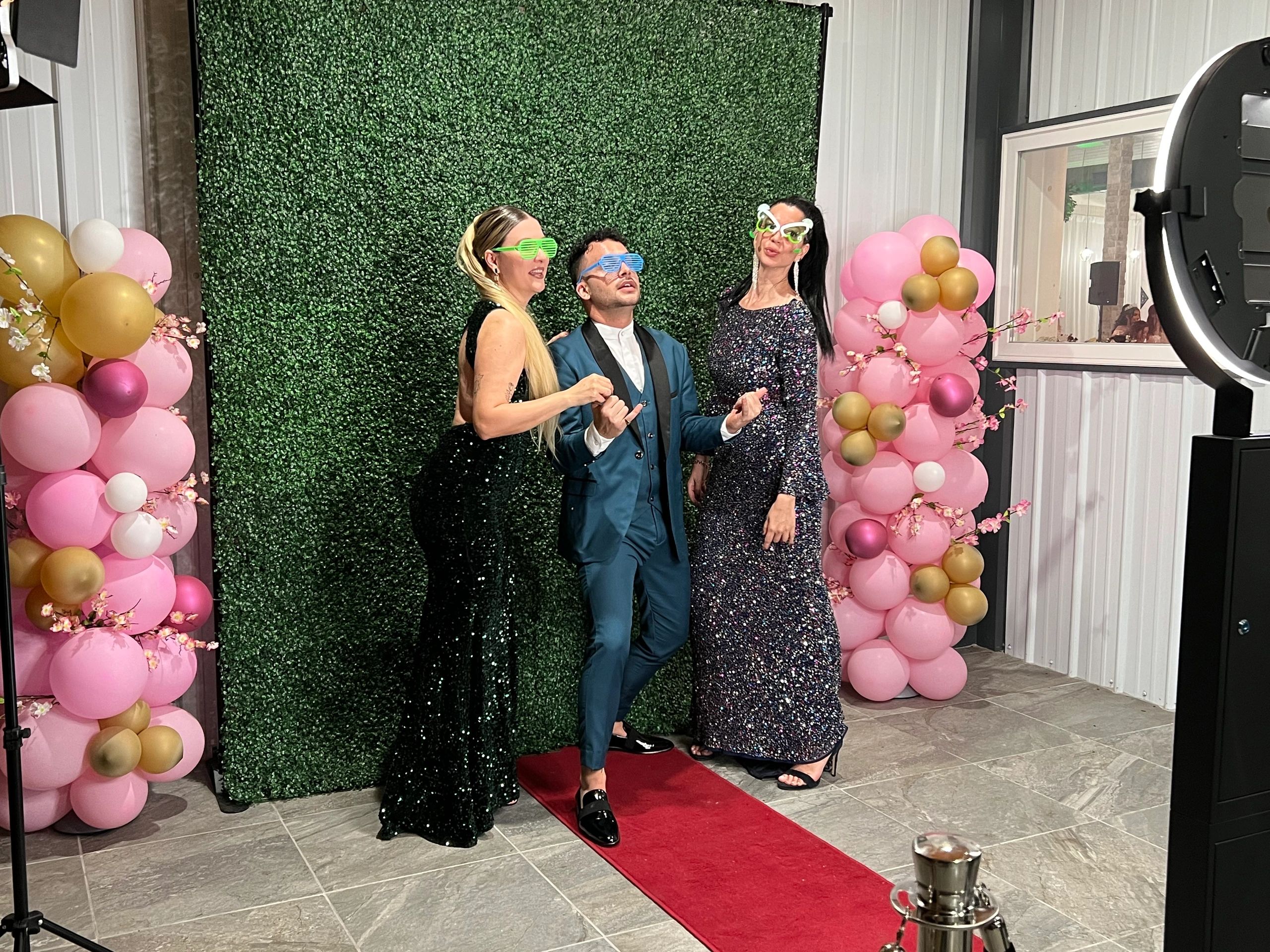 Posing for photo booth. Fun glasses props, grass wall backdrop & balloon arches.