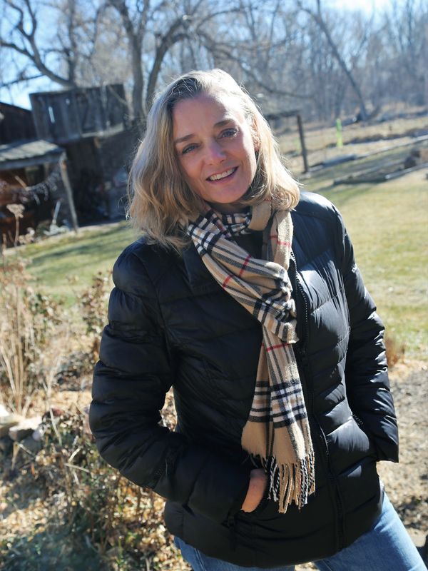 Woman in black jacket and plaid scarf smiling outdoors on a sunny day.